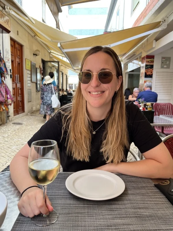 woman at restaurant table holding a glass of wine wearing sunglasses and black top