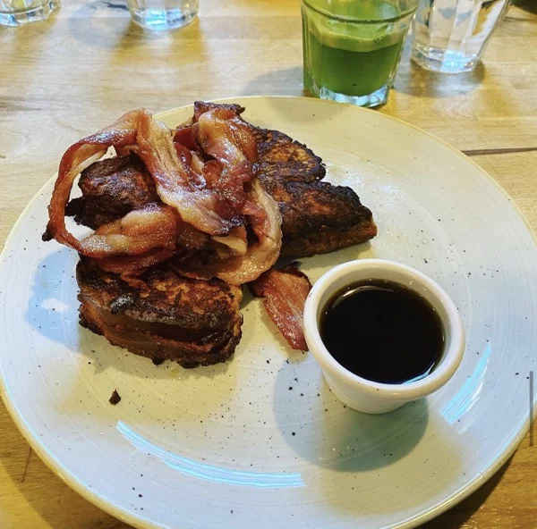 French toast with bacon with a side of maple syrup on a white plate 