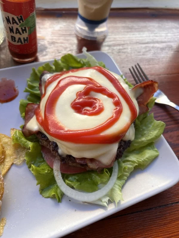 burger patty with melted cheese, tomato ketchup, onion and lettuce on a white plate